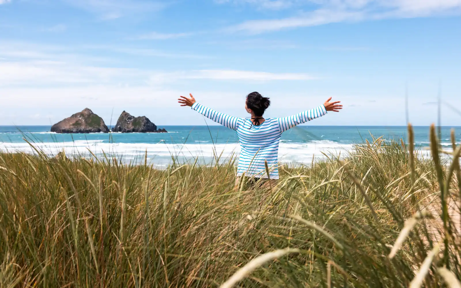 Woman standing in coastal dune grass with her arms raised at sunrise